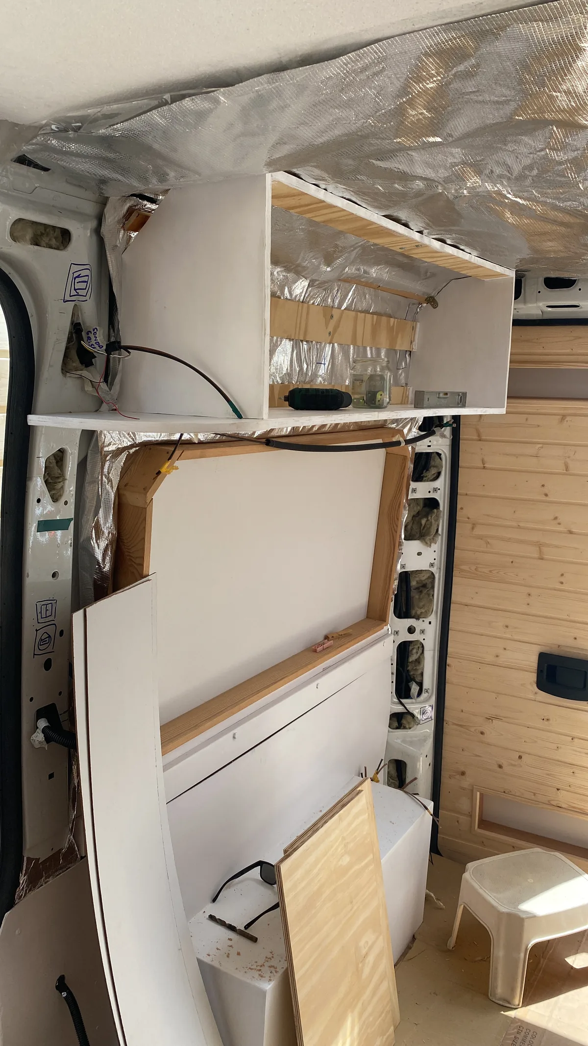 Interior de furgoneta overland en proceso de camperización con aislamiento, estructura de madera para estantes y herramientas
