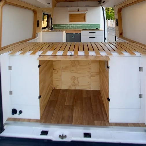 Furgoneta camper en proceso de conversión con base de cama de madera, espacio de almacenamiento y cocina con azulejos verdes