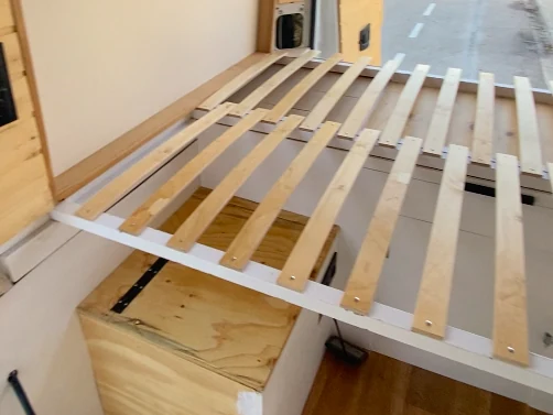 Cama de furgoneta camper con somier de lamas de madera y base de almacenamiento, mostrando el interior en construcción