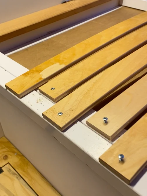 Detalle de listones de madera contrachapada atornillados sobre un marco blanco, construyendo el mobiliario de una van camper