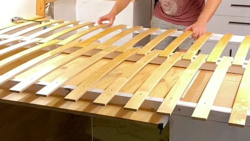 Manos construyendo una base de cama de listones flexibles de madera para furgoneta camper, proyecto de bricolaje vanlife