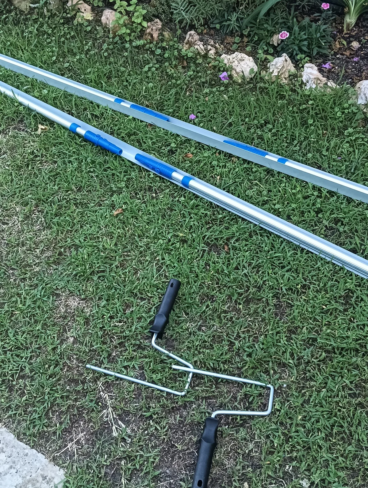 Dos pértigas extensibles de aluminio con detalles azules y dos soportes de rodillo de pintura sobre césped