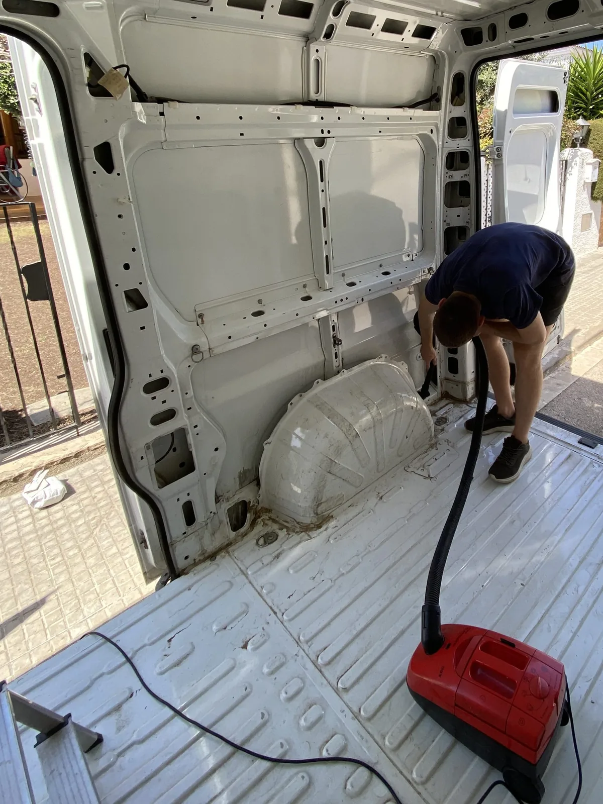 Persona limpiando el interior vacío de una furgoneta de carga blanca con aspiradora roja, primera fase de camperización