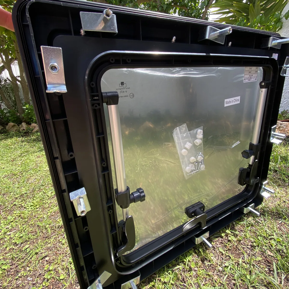 Ventana abatible negra para furgoneta camper, mostrando soportes regulables y kit de montaje en el exterior para overland