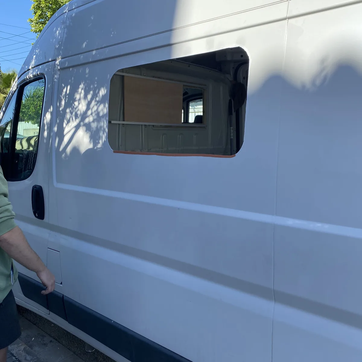 Hueco de ventana recién cortado en furgoneta blanca, mostrando armazón de madera inicial para la conversión camper overland