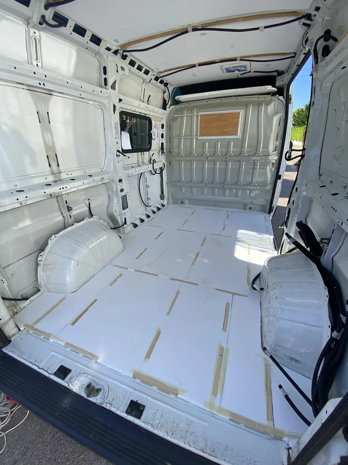 Interior de furgoneta blanca para camperizar con aislamiento de suelo, listones de madera, ventana y claraboya