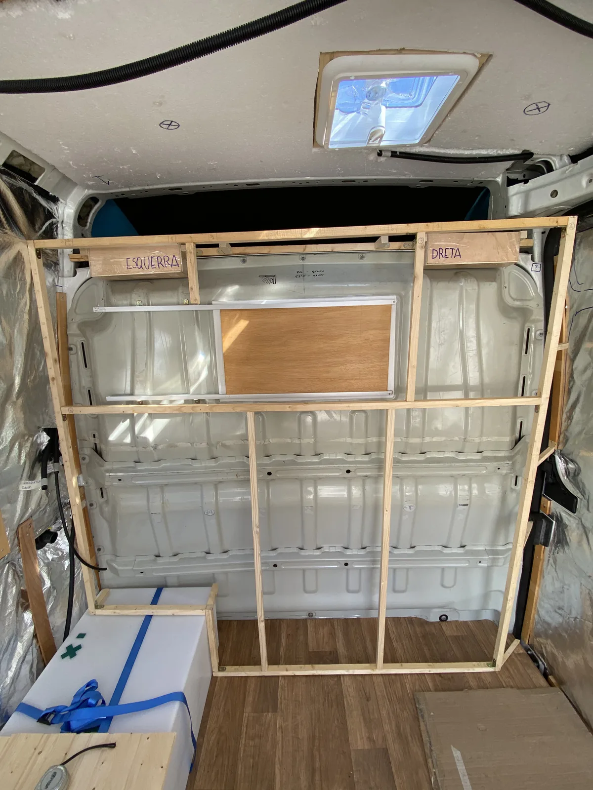 Interior de furgoneta camperizándose con estructura de madera, aislamiento térmico y depósito de agua para viajes overland