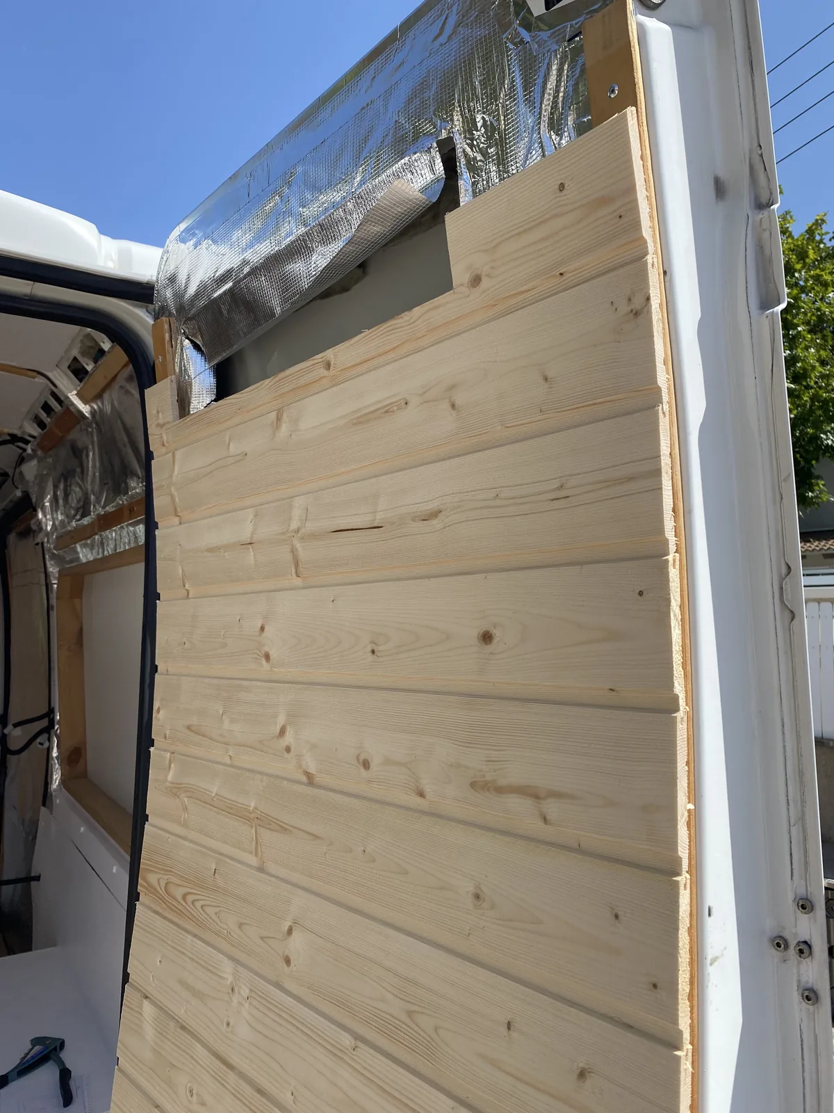 Detalle de paneles de madera de pino machihembrada instalándose en el interior de una furgoneta camperizada con aislante
