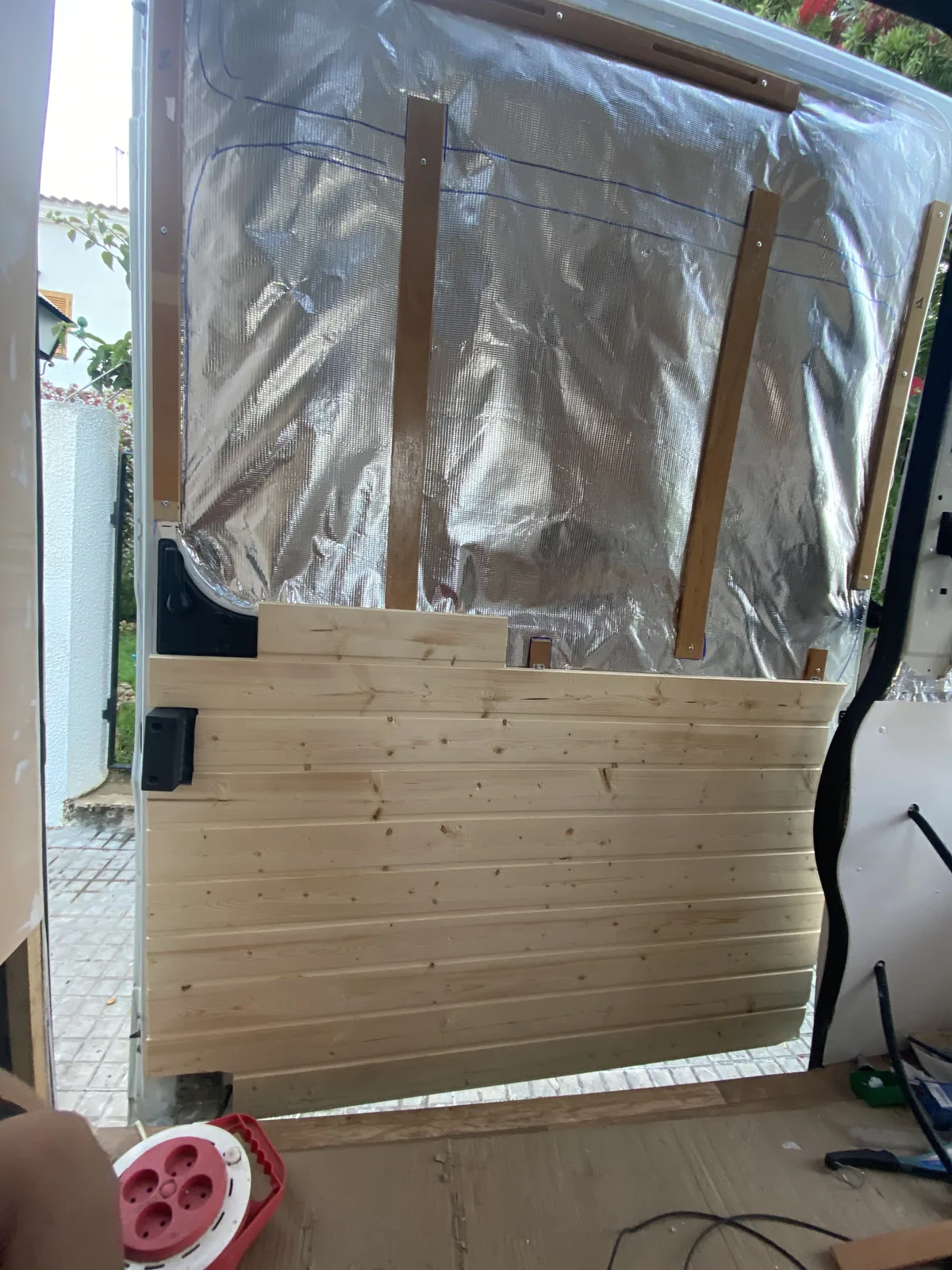 Interior de furgoneta camper: Puerta trasera con aislamiento térmico plateado y panelado de madera natural en montaje