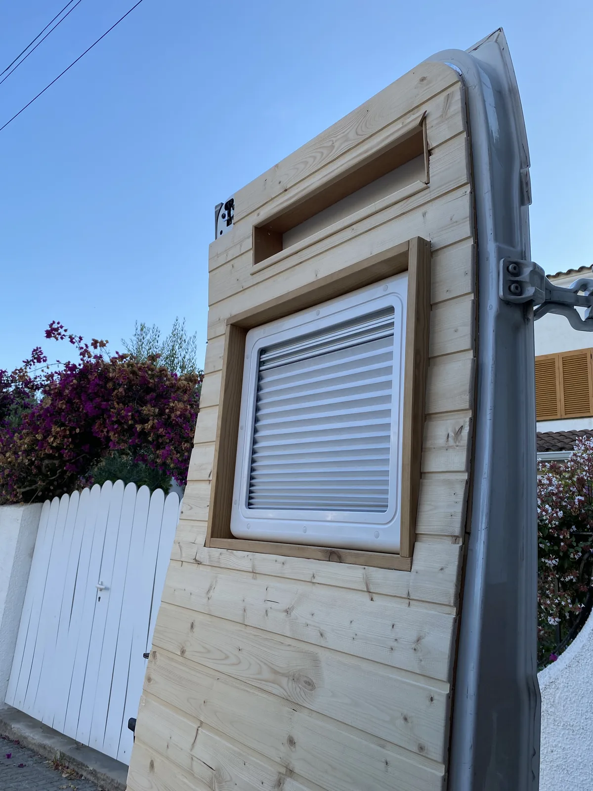 Panelado de madera en el lateral de una furgoneta camper en proceso de camperización, con ventana de caravana instalada