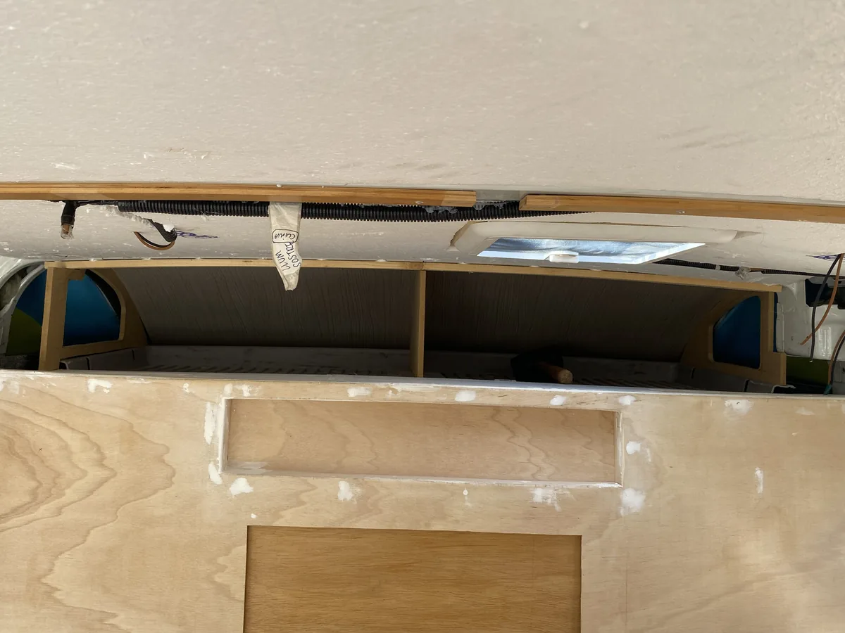 Interior de furgoneta overland en proceso de camperización con paneles de madera contrachapada, techo y cableado expuesto