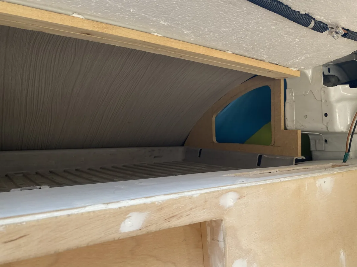 Detalle de la conversión de furgoneta overland con estructura de madera, aislamiento en el techo y el paso de rueda visible
