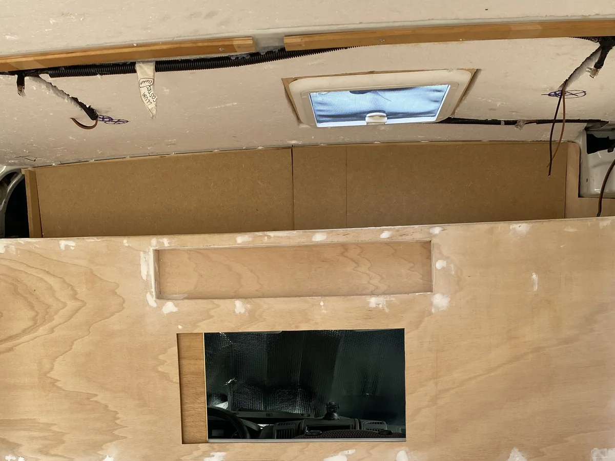 Proceso de camperización de furgoneta overland con paneles de contrachapado de madera, masilla y claraboya en el techo