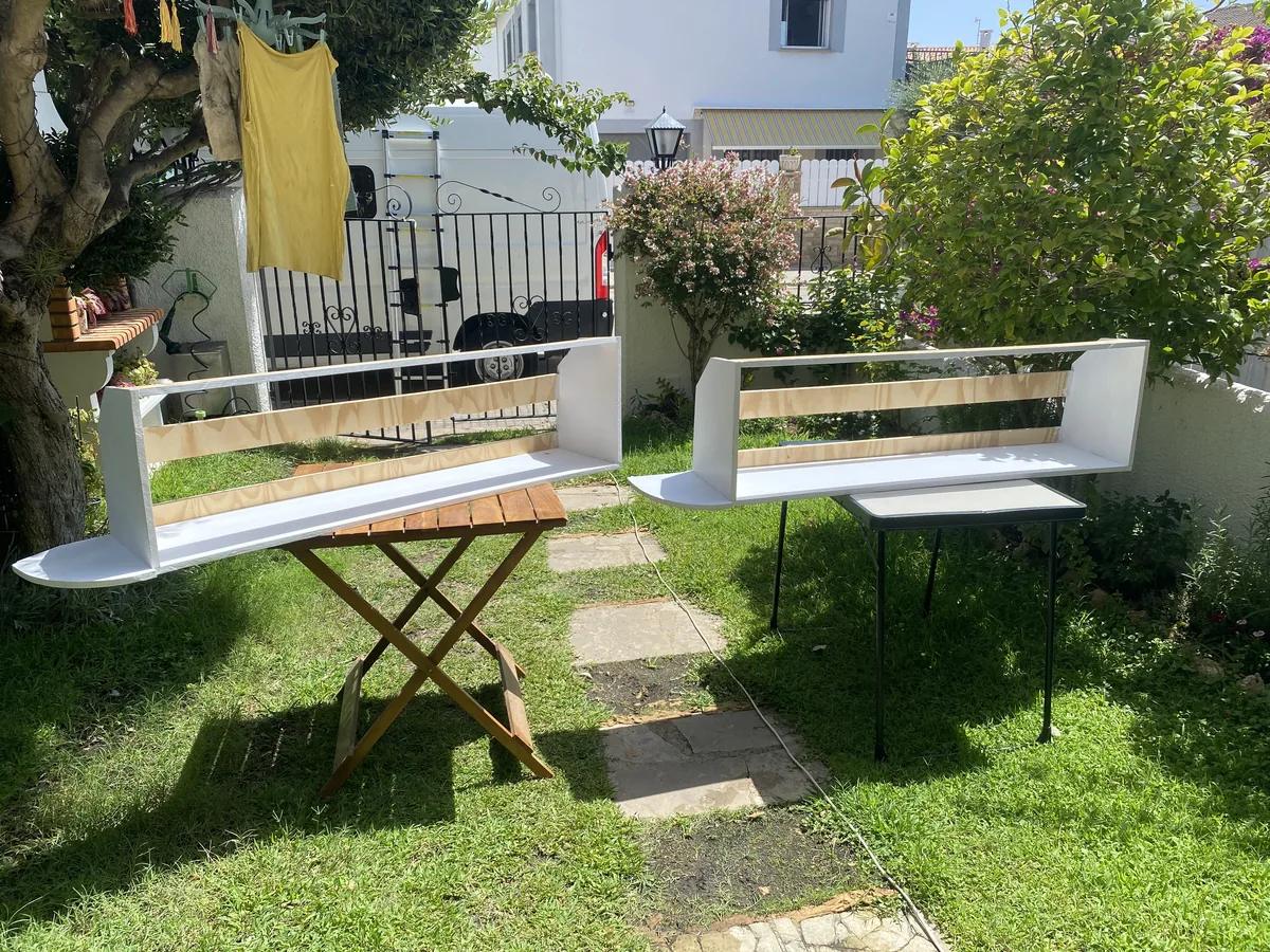 Estanterías de madera blancas recién pintadas secándose en el jardín, con la furgoneta camper al fondo, para nuestro proyecto