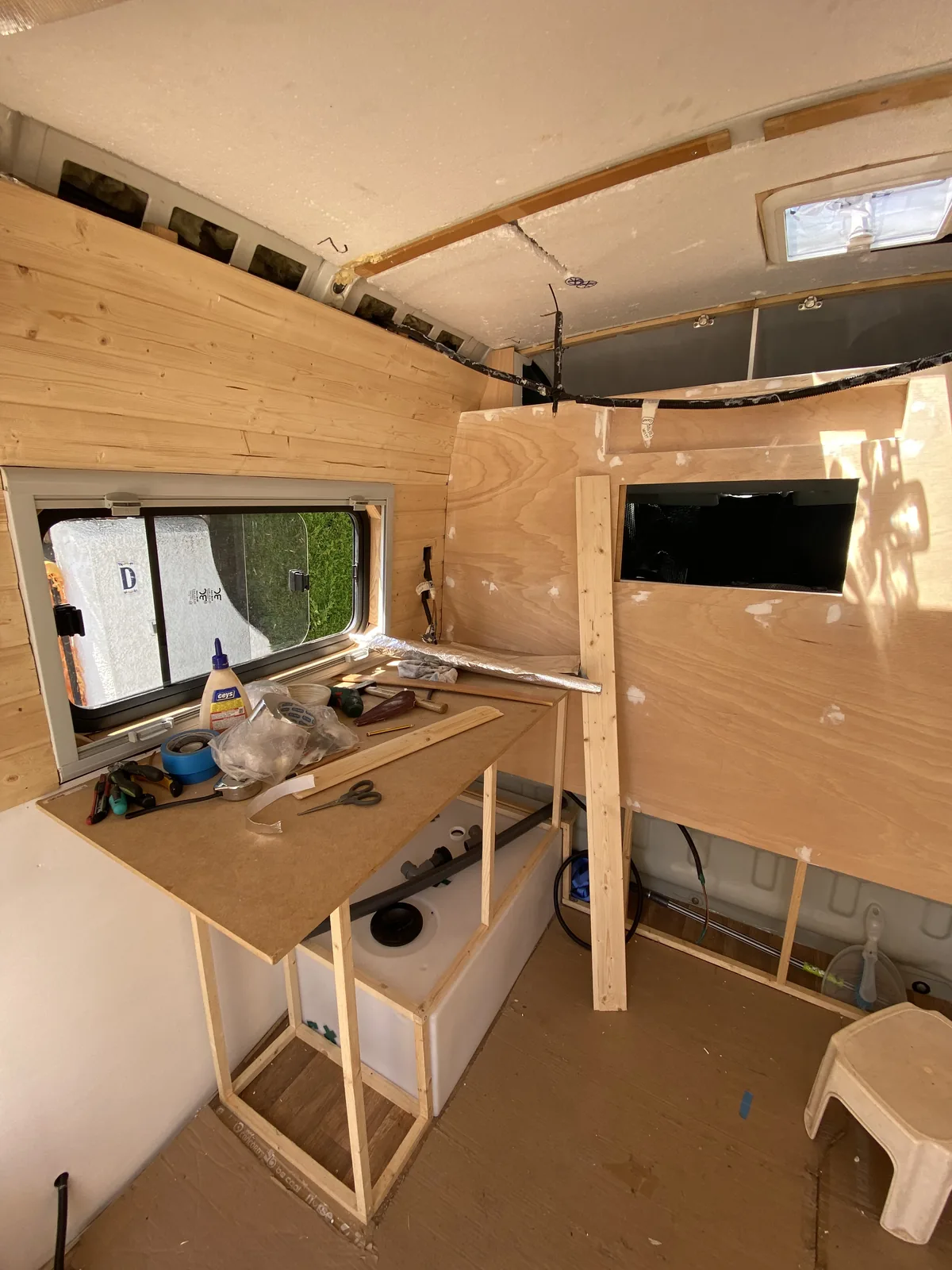 Construcción interior de furgoneta camper overland con paneles de madera, ventana, tanque de agua y herramientas