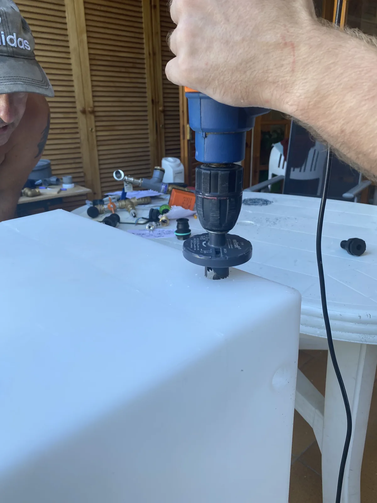 Perforando un depósito de agua blanco con taladro para el sistema de agua de una furgoneta camper overland