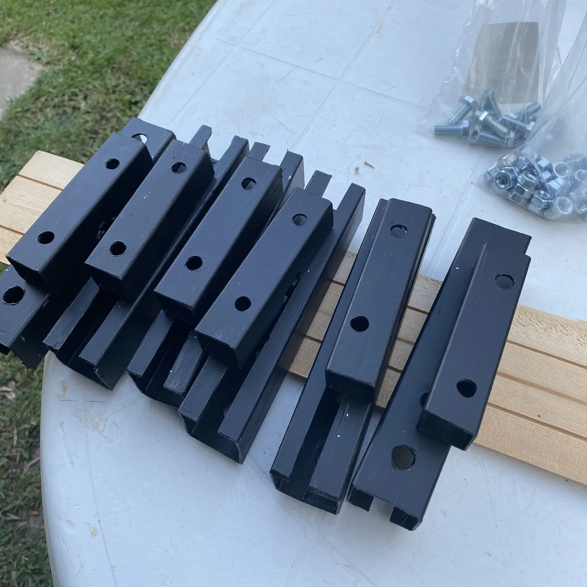 Soportes de metal negros con agujeros, preparados para instalar equipamiento overland en van, junto a bolsas de tornillos
