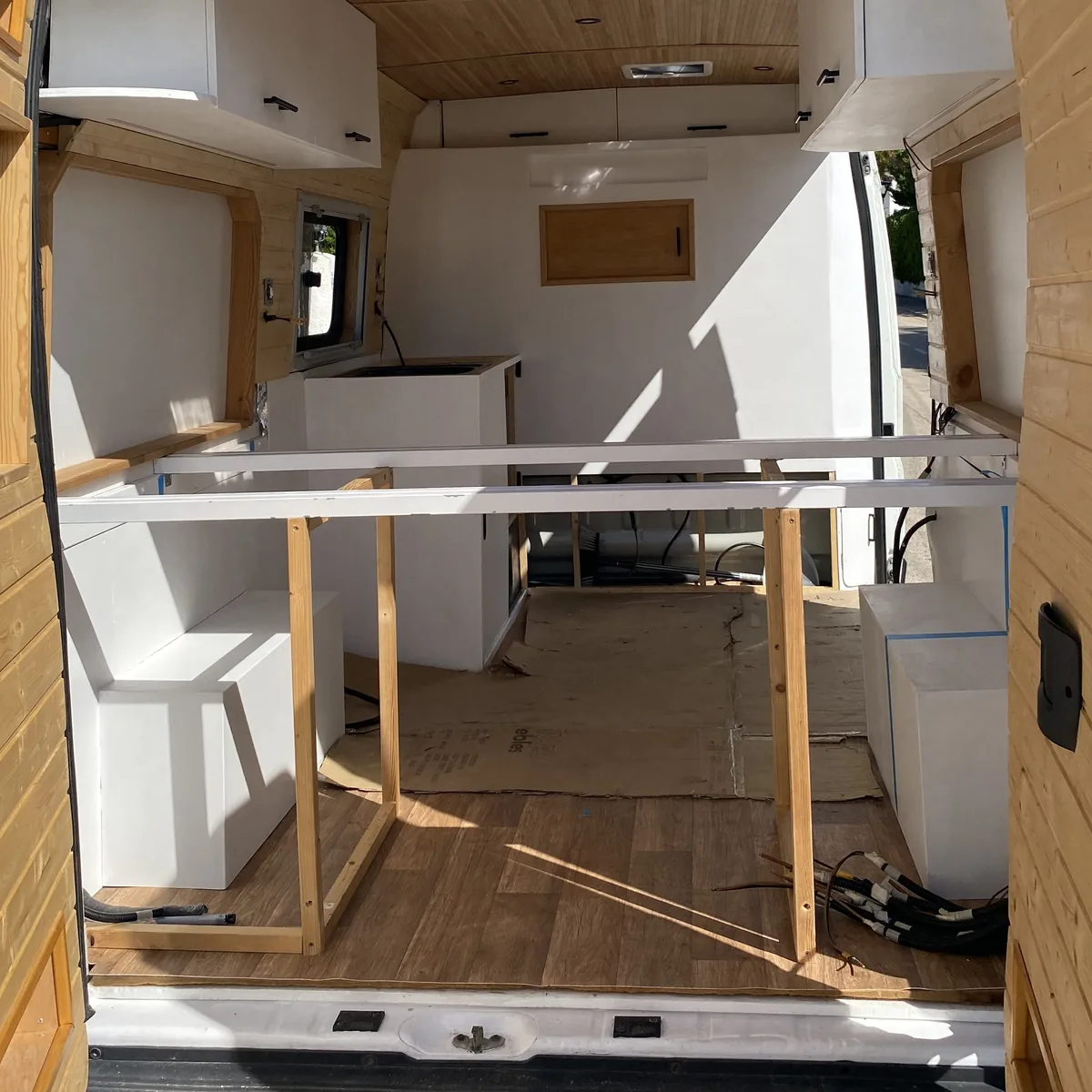 Furgoneta camper en plena camperización, con estructura de muebles blancos, techo de madera y suelo laminado