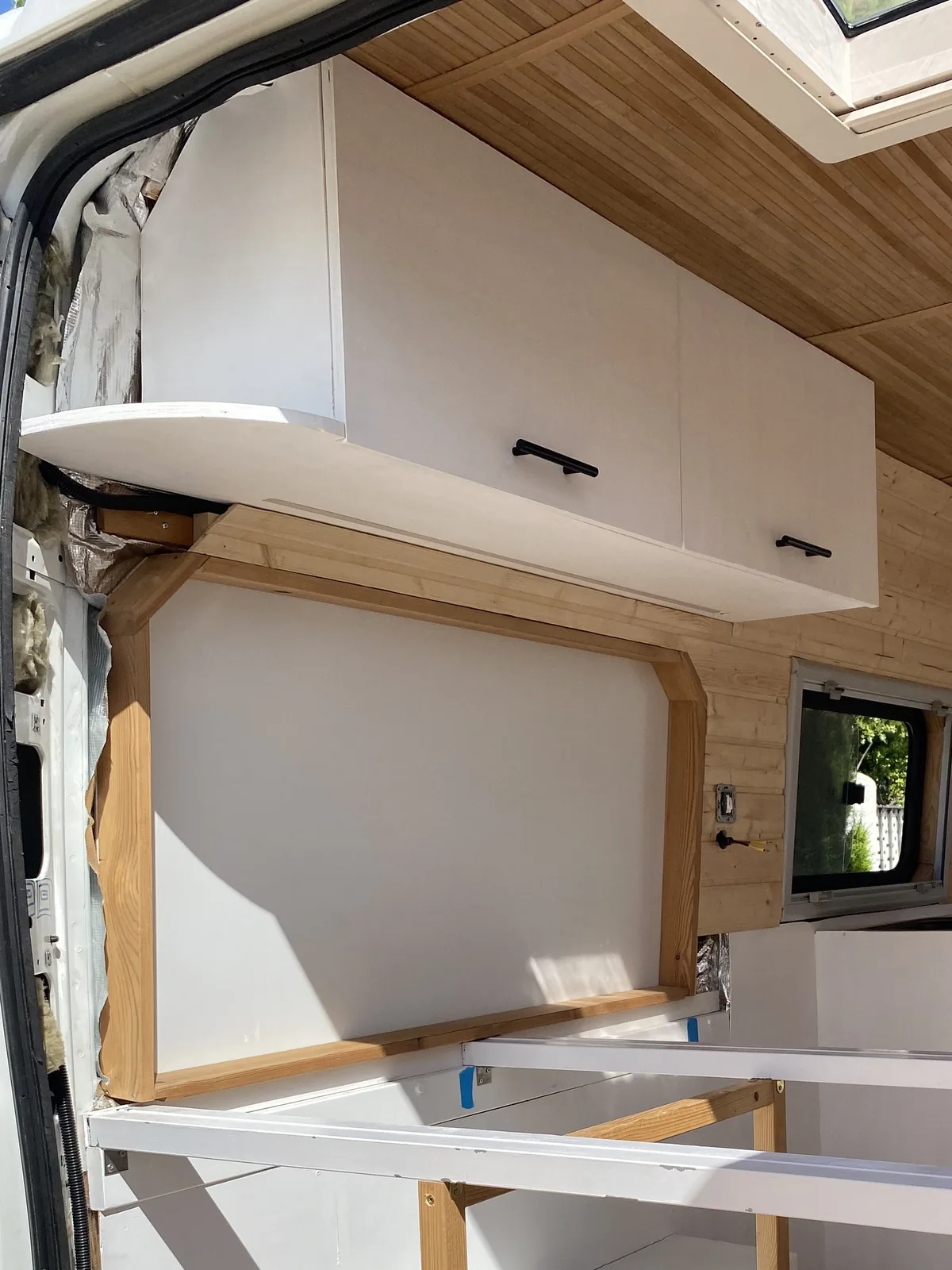 Proceso de camperización de furgoneta: interior con armarios blancos, techo de madera y base de cama en construcción