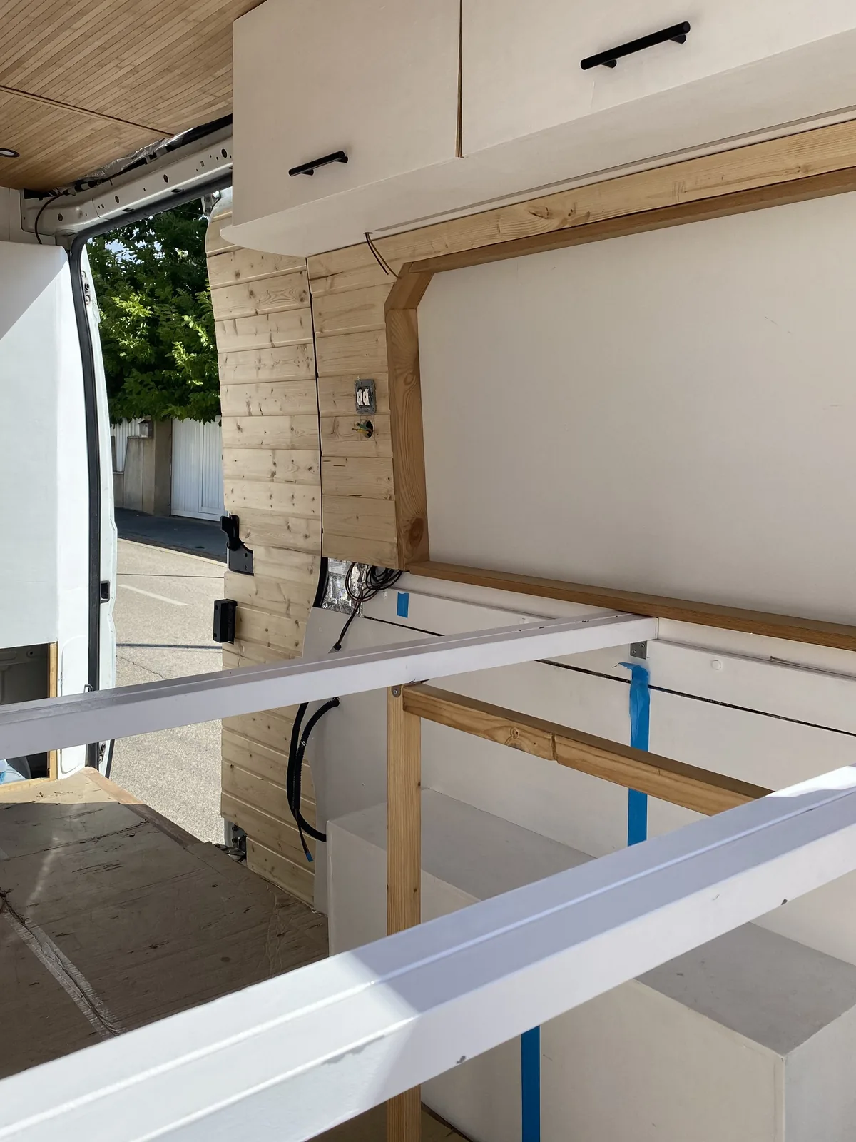 Interior de furgoneta overland en camperización DIY. Detalles de madera, gabinetes superiores y estructura de cama metálica
