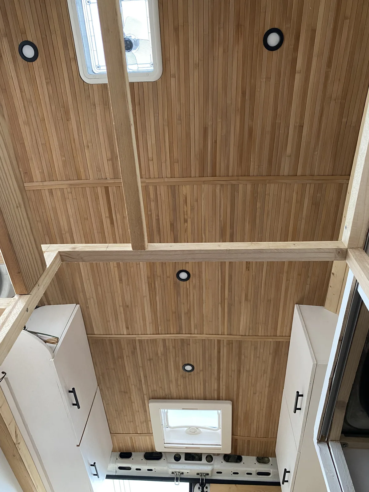 Interior de furgoneta overland con techo de listones de madera, dos claraboyas con ventilador y luces LED empotradas