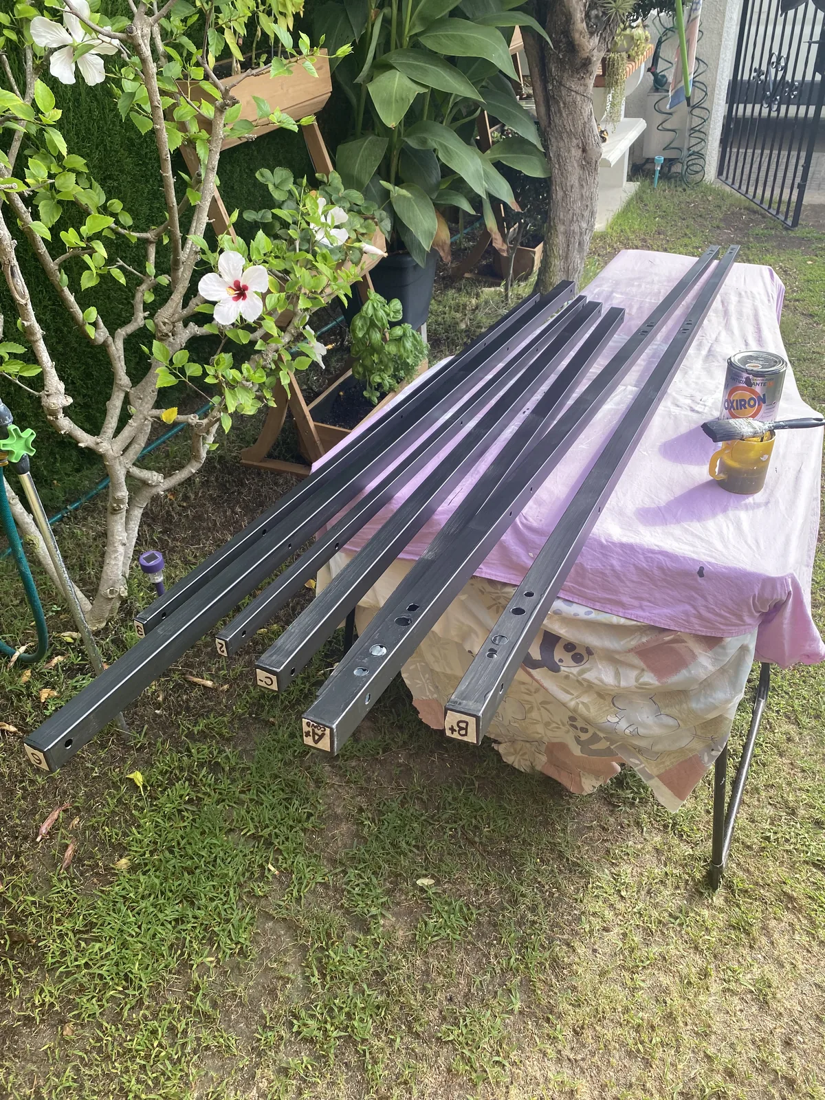 Piezas metálicas cuadradas, recién pintadas de gris oscuro con Oxiron en un jardín, para la estructura exterior de una van