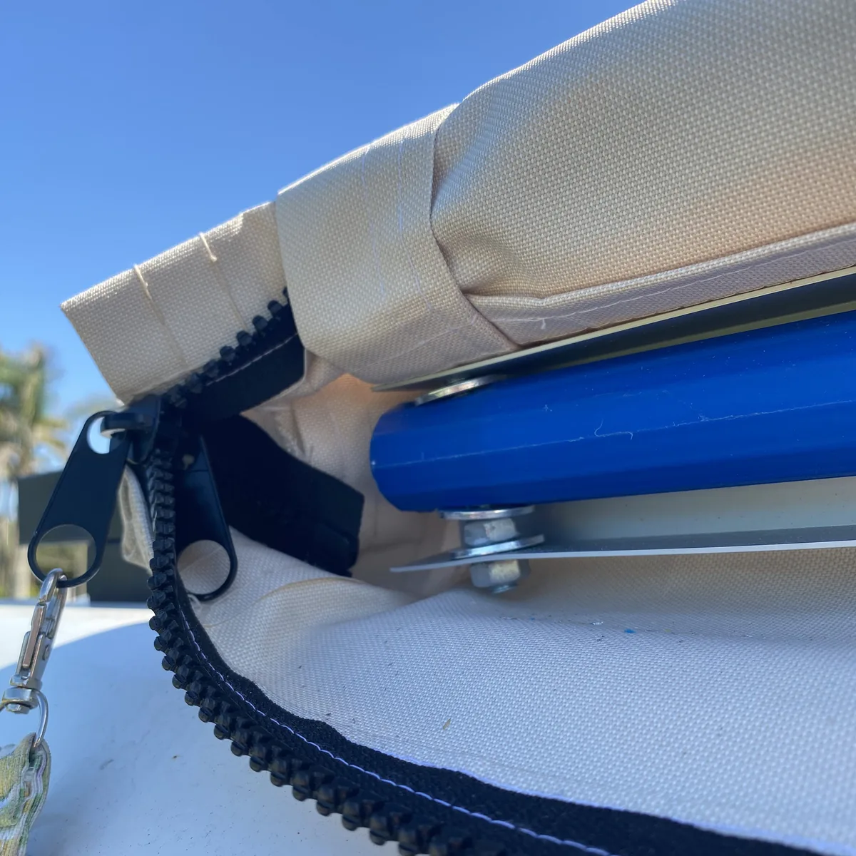Toldo de van overland enrollado en funda beige con cremallera, mostrando poste azul y herrajes bajo cielo despejado