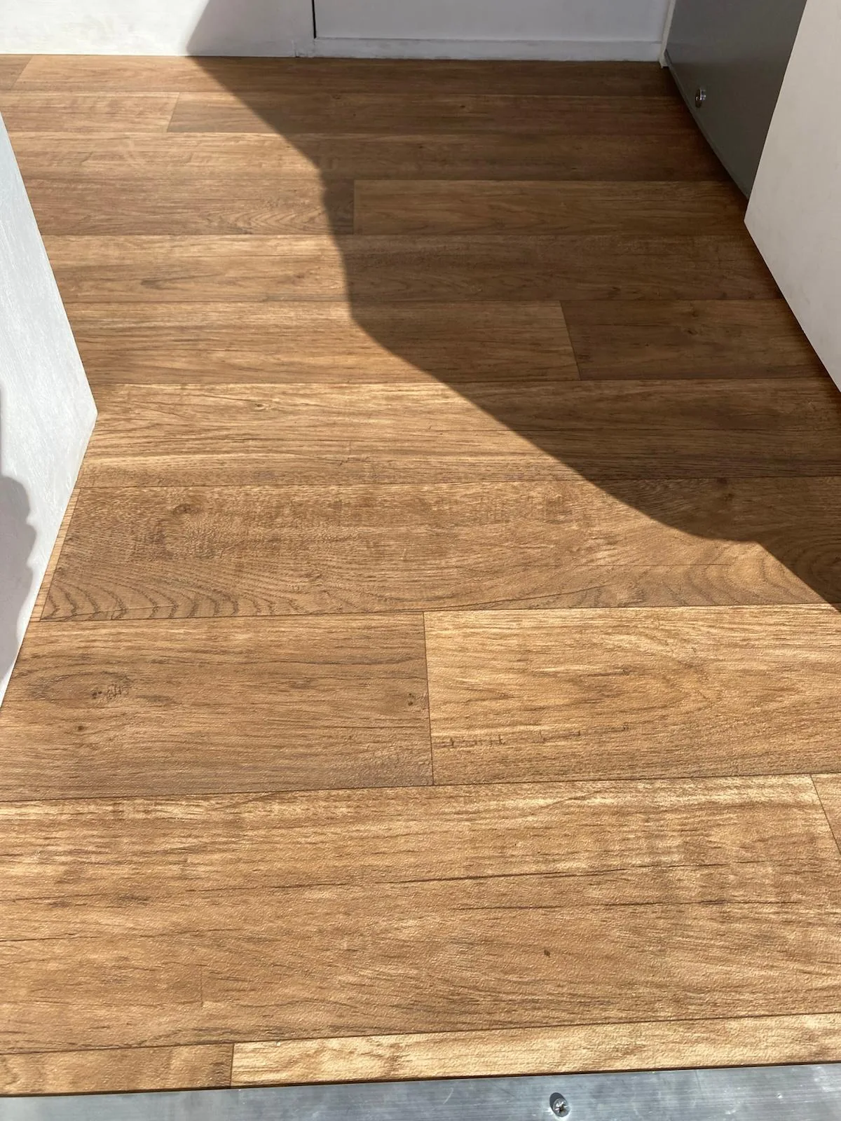 Detalle del suelo de vinilo tipo madera claro con vetas, instalado en el interior de una furgoneta camper overland