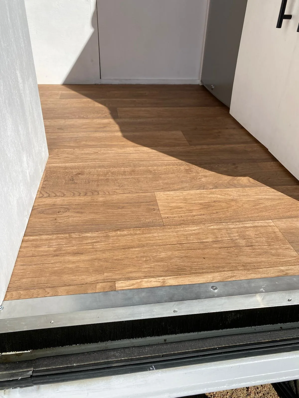 Suelo vinílico efecto madera y umbral metálico con cepillo aislante en la entrada de una furgoneta camper para overland