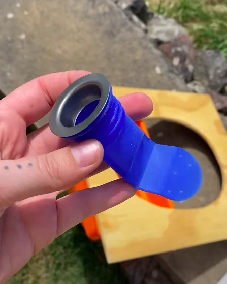 Mano sosteniendo una válvula antirretorno de silicona azul, listo para usar con un asiento de inodoro de madera