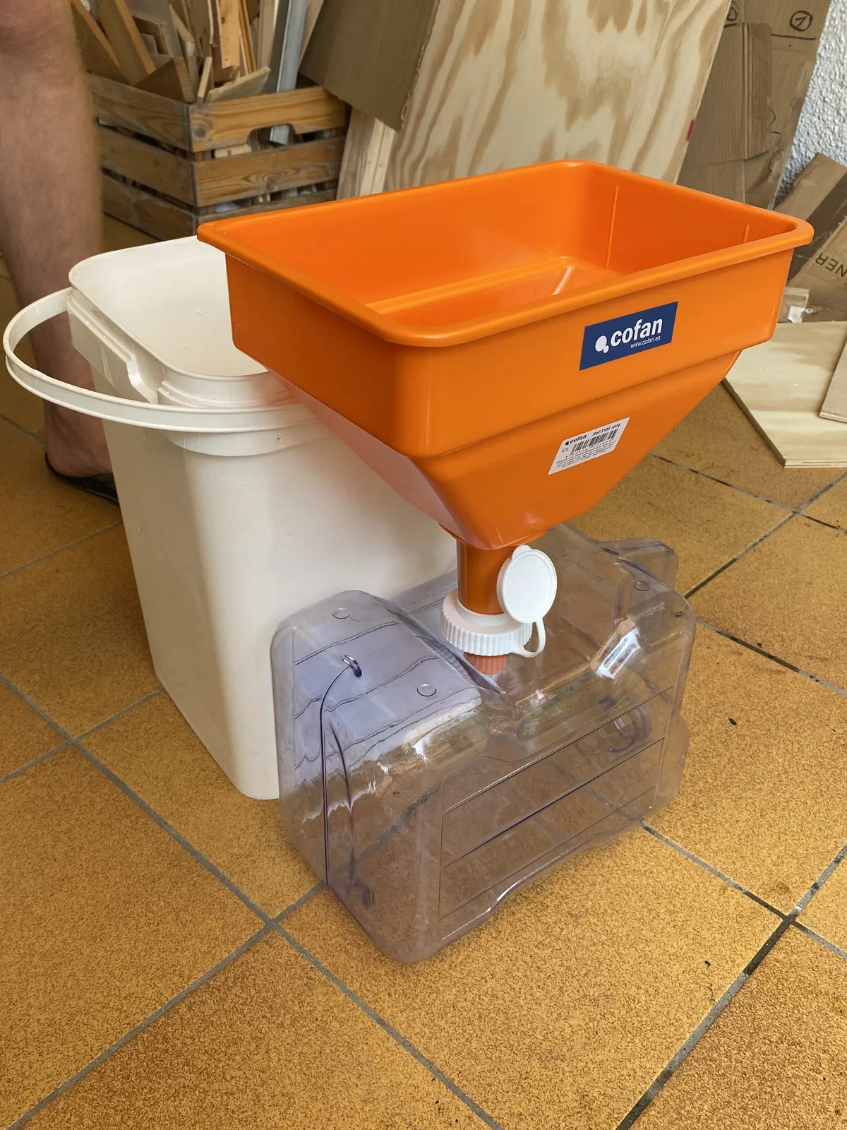 Detalle de equipo para gestionar el baño en van: embudo naranja Cofán sobre garrafa transparente junto a un cubo blanco