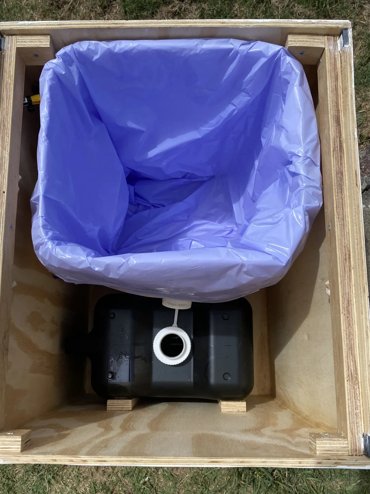 Inodoro seco DIY para furgoneta camper: caja de madera, bolsa morada y depósito de residuos negro en la base