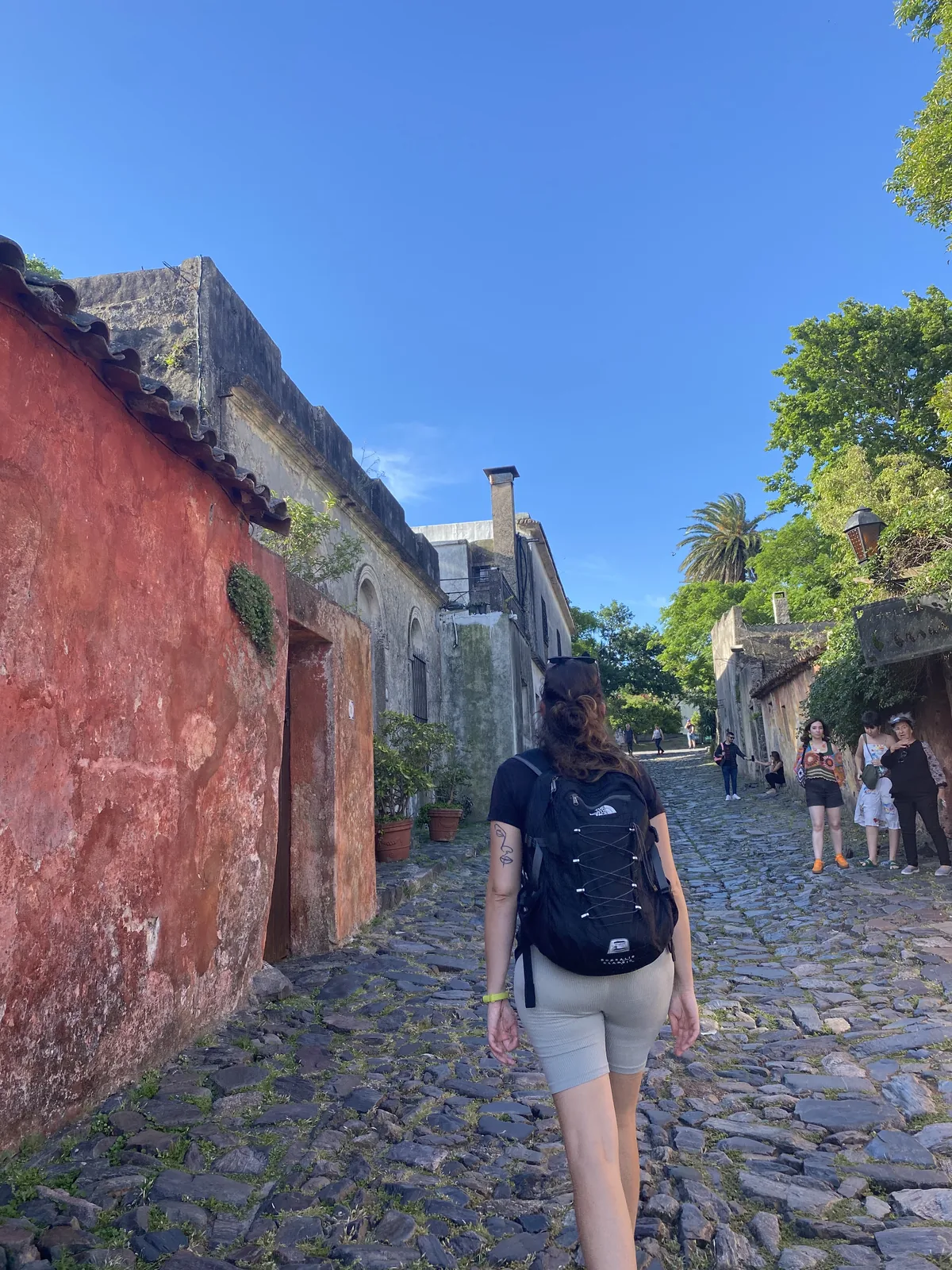 Viajera con mochila The North Face recorre calle empedrada en casco histórico de Colonia del Sacramento, Uruguay