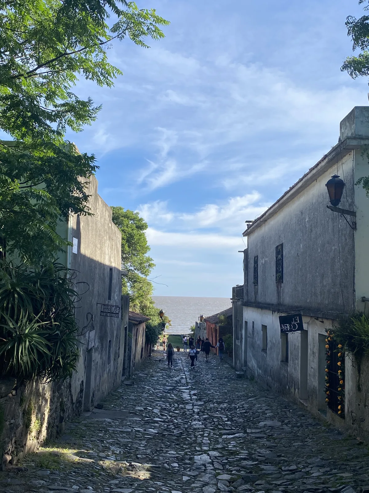 Calle de adoquines empedrada en Colonia del Sacramento, Uruguay, con edificios históricos a los lados y el Río de la Plata