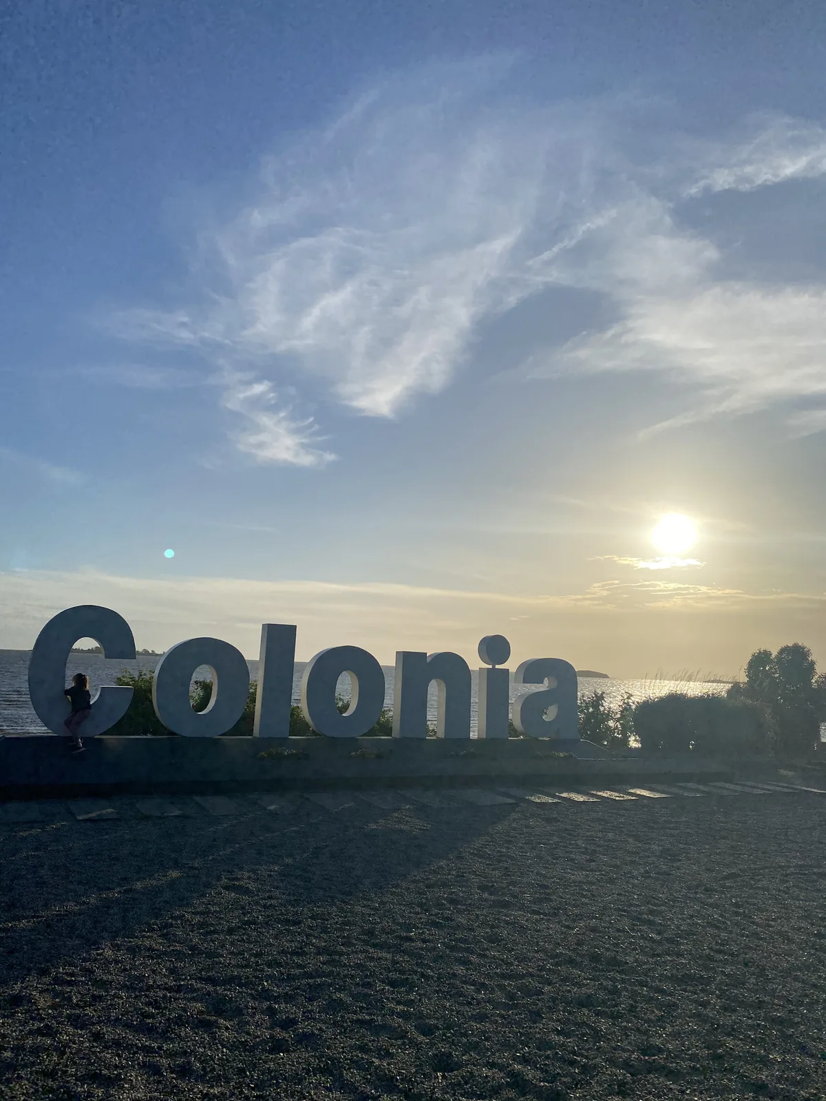 Letras gigantes de Colonia al atardecer sobre el Río de la Plata, bajo un cielo azul con nubes tenues