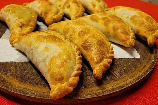 Múltiples empanadas caseras de masa dorada con su característico repulgue, servidas en una tabla rústica de madera