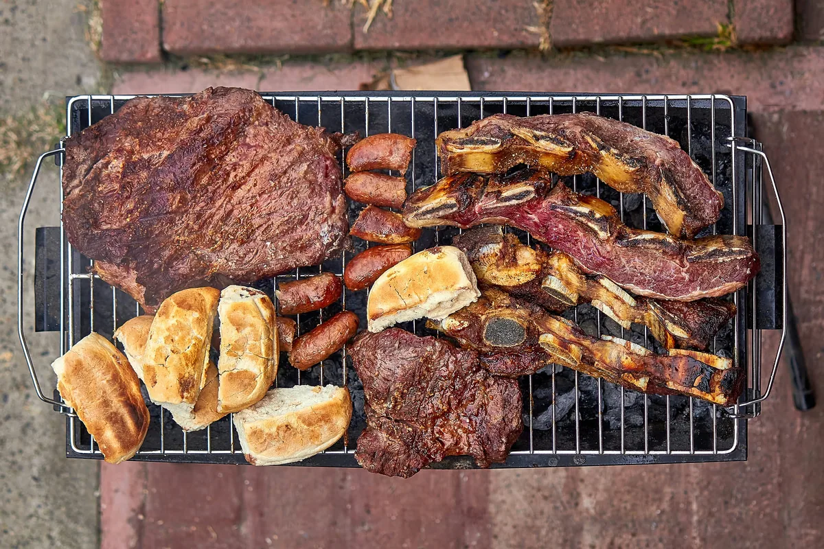 Asado tradicional argentino con costillar, vacío, chorizos y panes en parrilla portátil