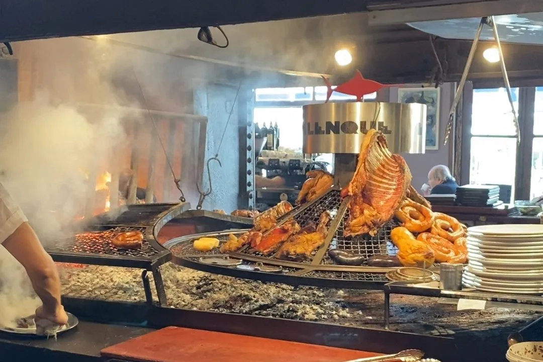 Gran parrilla de restaurante con chef asando costillar de cordero, chorizos y morcillas entre humo y brasas