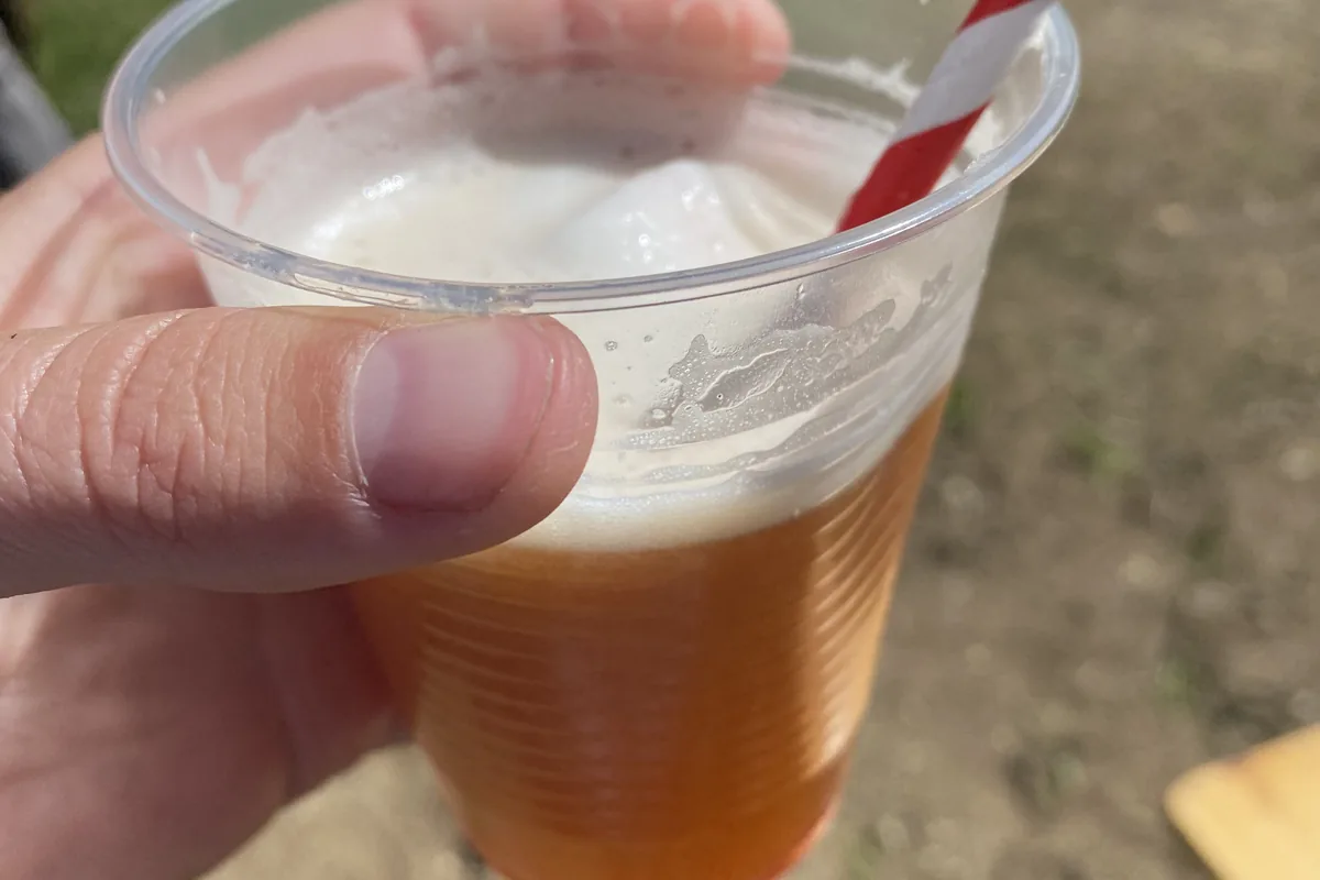 Mano sosteniendo refresco espumoso en vaso de plástico con pajita a rayas, disfrutado durante un descanso overland