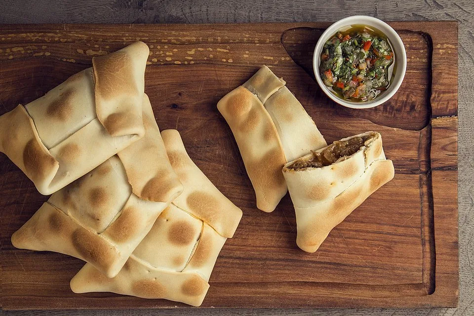 Empanadas argentinas de carne con chimichurri en tabla de madera, una partida revelando el jugoso relleno