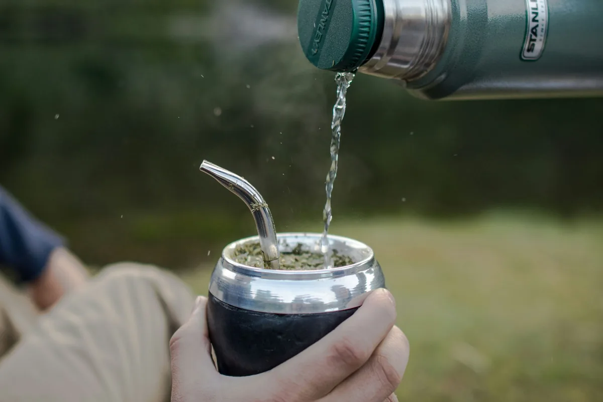Overlander sirviendo mate caliente de un termo Stanley en la naturaleza, pausa en la ruta