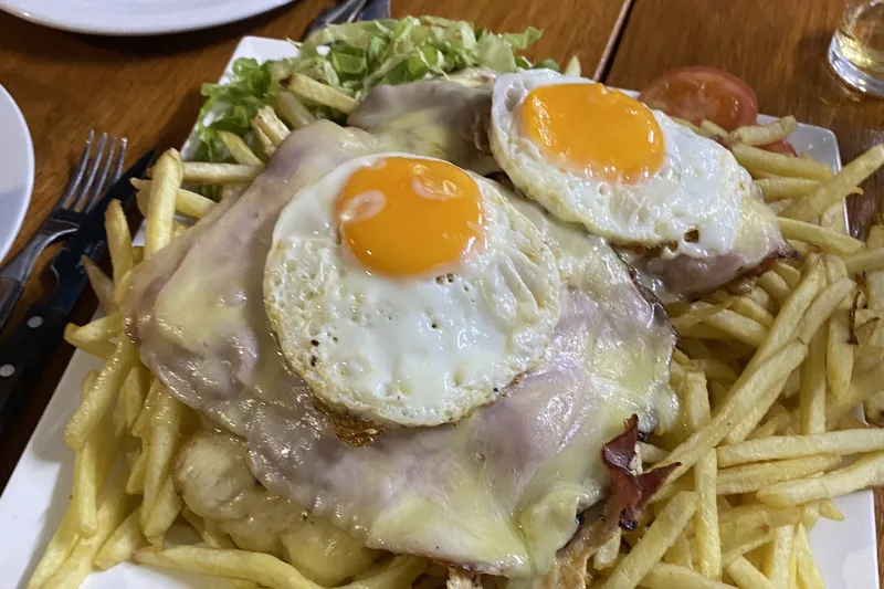 Plato de milanesa con jamón, queso fundido, dos huevos fritos y papas fritas en una mesa de madera durante un viaje