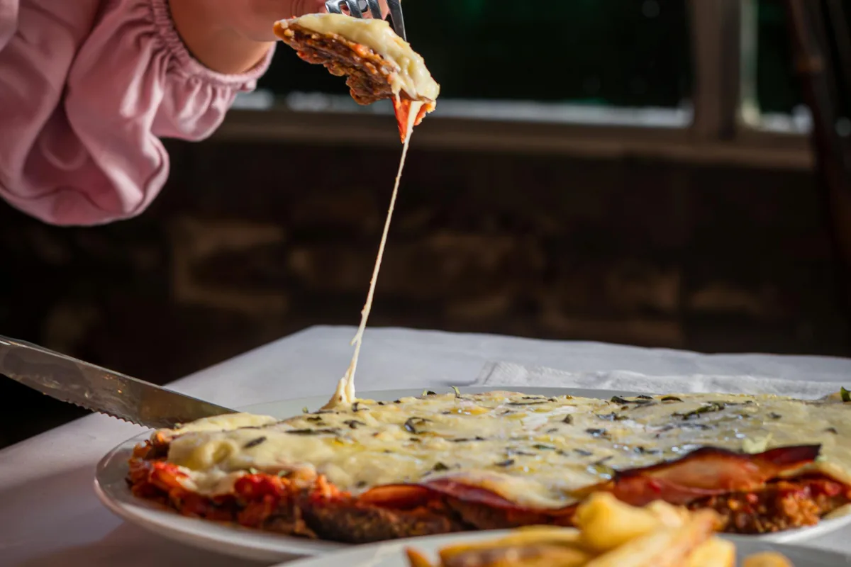 Sirviendo una generosa porción de milanesa napolitana con mucho queso fundido estirándose y patatas fritas