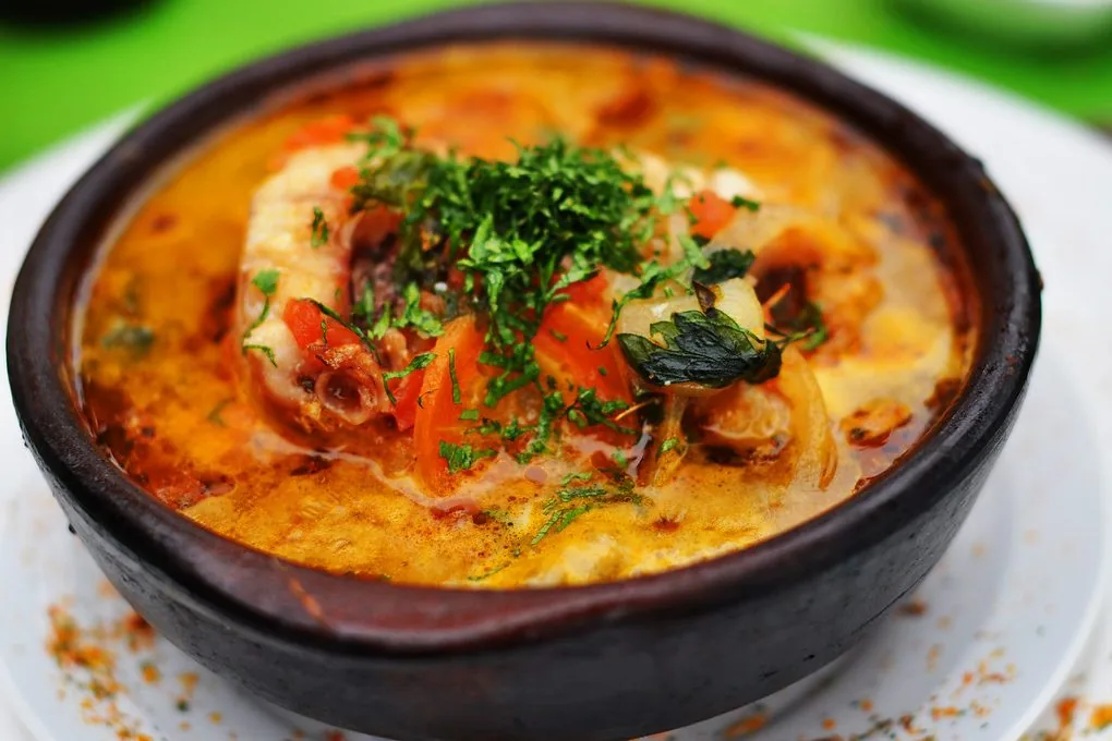 Colorido guiso de pescado con tomate, cebolla y hierbas frescas servido en cazuela de barro, una experiencia culinaria