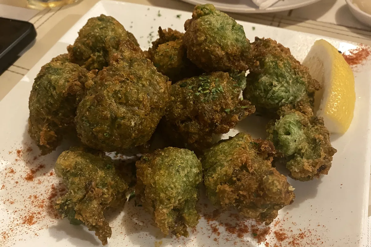 Buñuelos verdes fritos, con textura crujiente, servidos en plato blanco con limón y pimentón espolvoreado