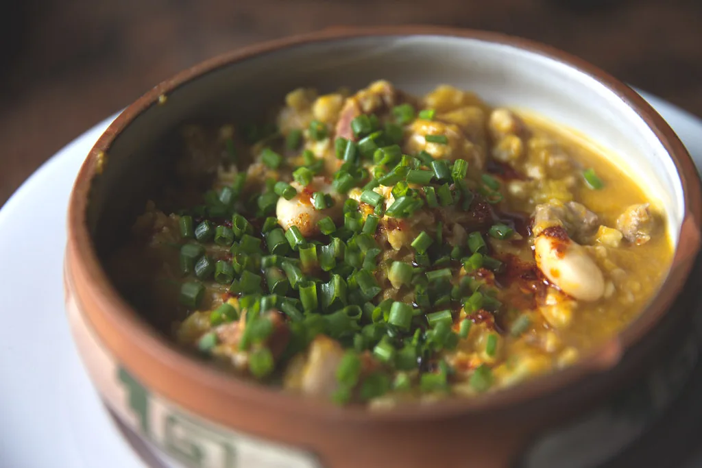 Guiso de maíz, porotos y carne con cebollino en cuenco de barro. Comida tradicional en ruta overland