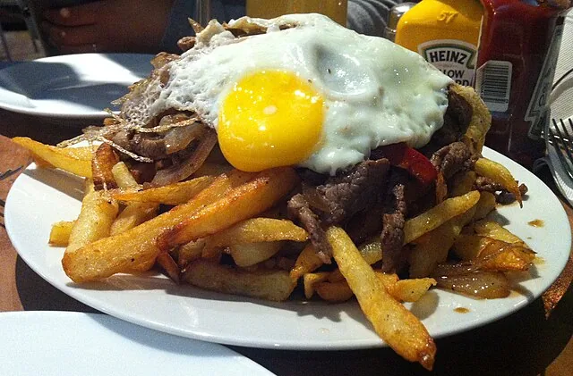 Abundante plato con papas fritas, carne salteada, cebolla, pimientos y huevo frito, recargando energías en ruta por Sudaméric