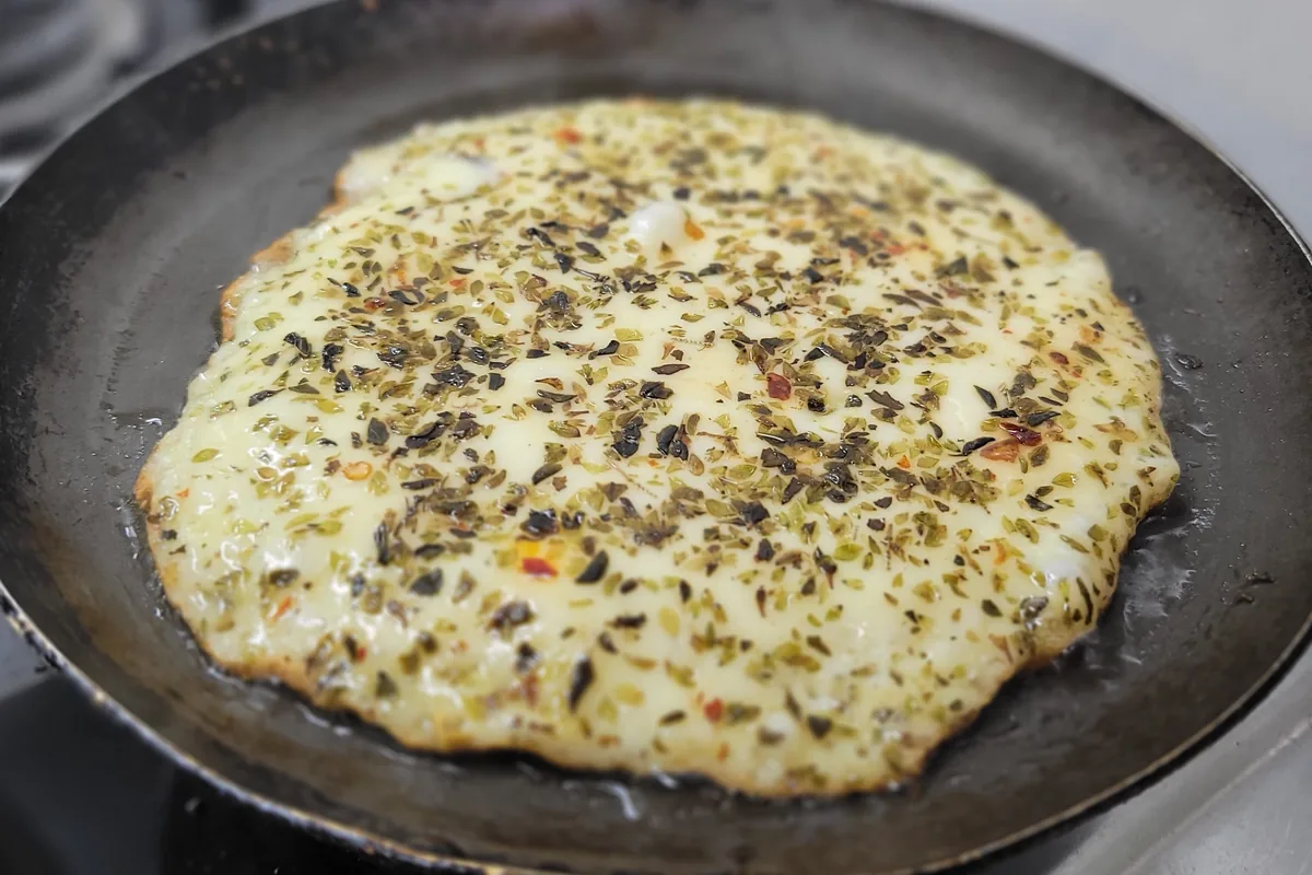 Provoleta argentina con orégano derritiéndose en una sartén sobre la cocina de nuestra van, lista para un festín rodante