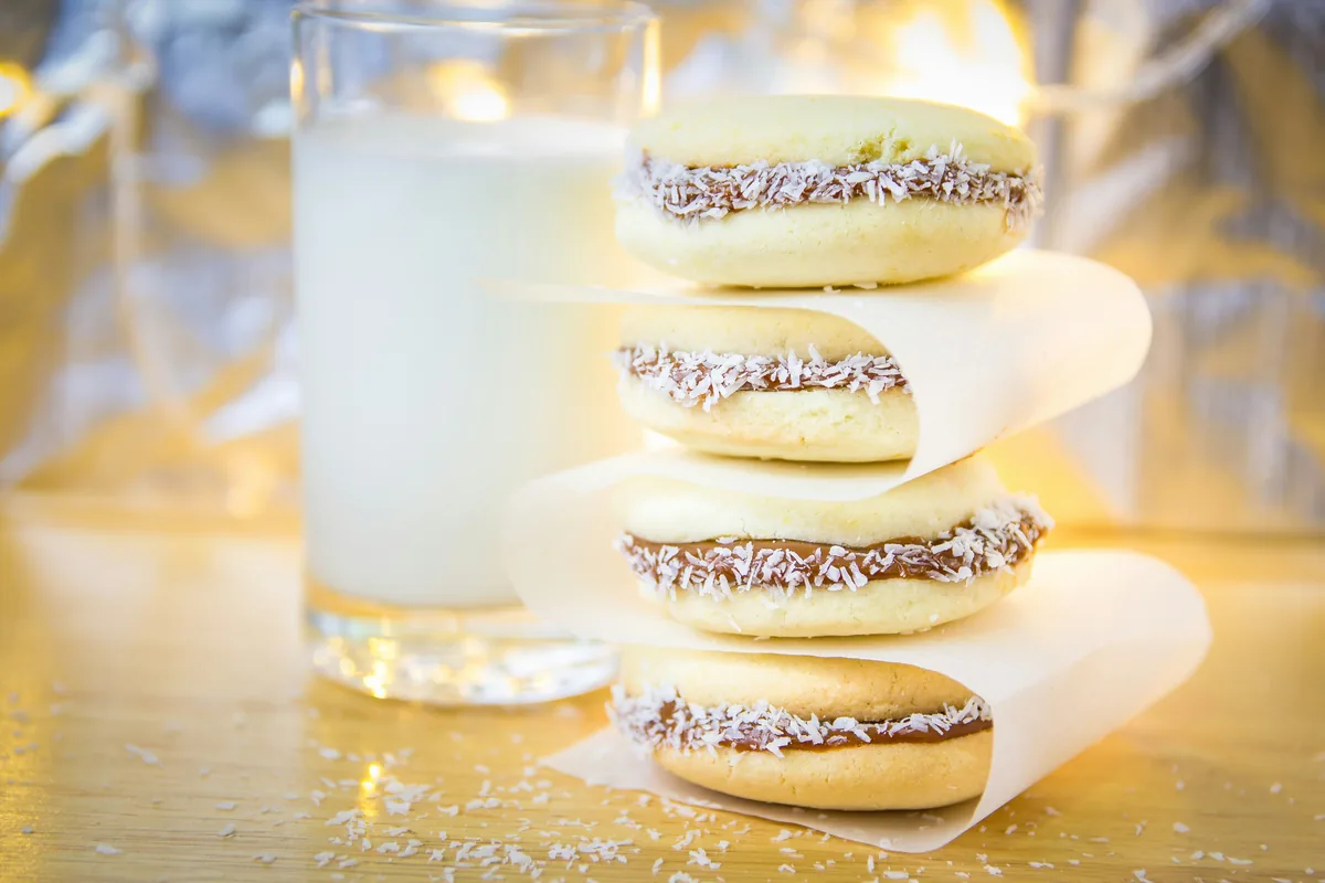 Alfajores de dulce de leche con coco rallado, apilados junto a un vaso de leche. Un dulce perfecto para la ruta