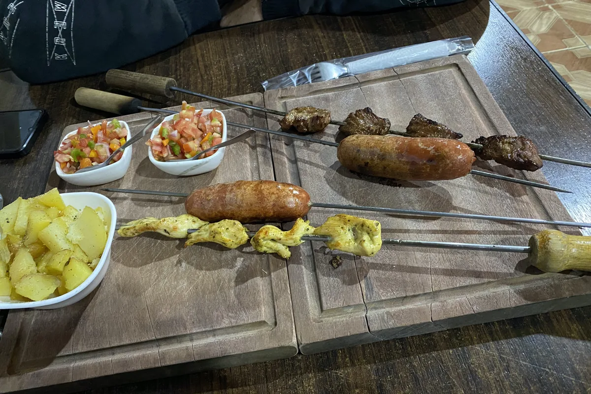 Sabrosa parrillada con brochetas de res, pollo, chorizos, papas y salsa criolla servida en tablas rústicas de madera